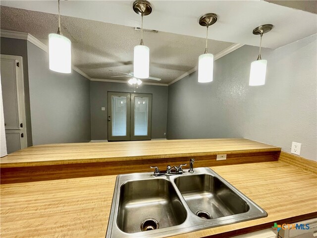 kitchen featuring sink, ornamental molding, ceiling fan, wood-type flooring, and pendant lighting