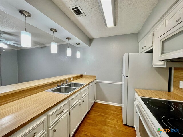 kitchen with light wood-type flooring, a textured ceiling, pendant lighting, white cabinets, and white appliances