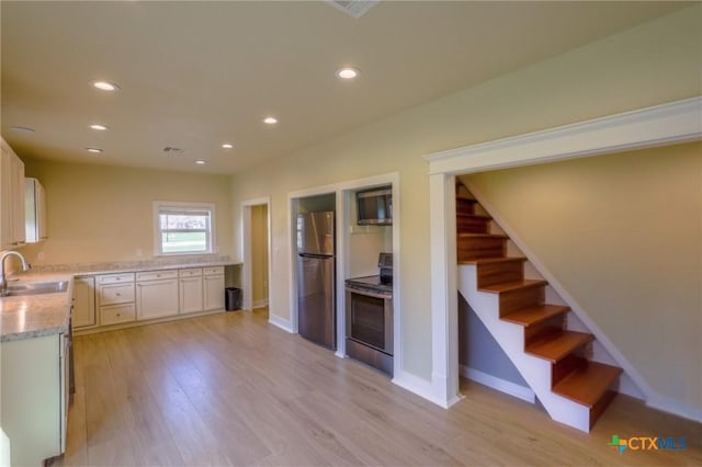 kitchen featuring recessed lighting, light stone countertops, a sink, stainless steel appliances, and light wood-style floors