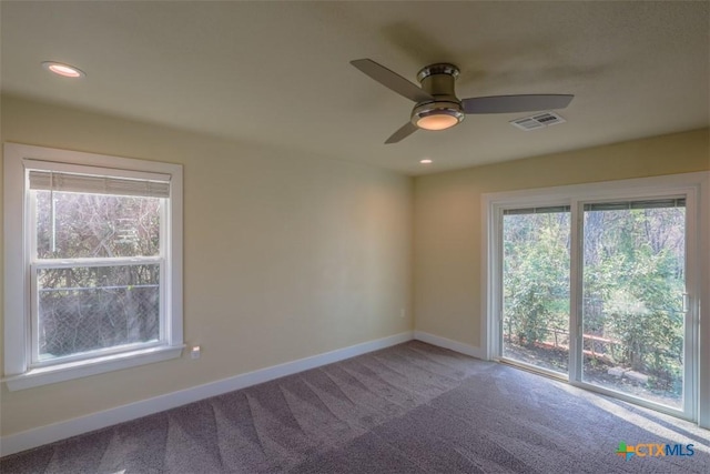 carpeted spare room featuring baseboards, visible vents, a ceiling fan, and plenty of natural light