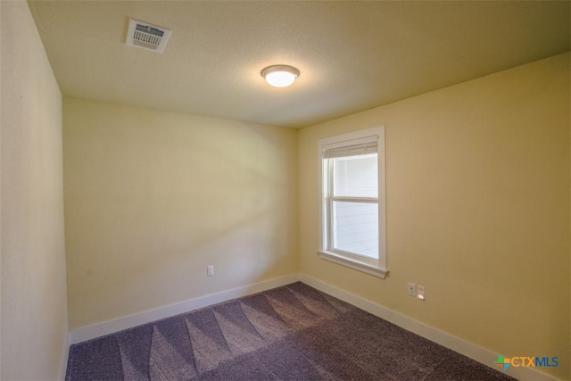 spare room featuring visible vents, dark colored carpet, and baseboards