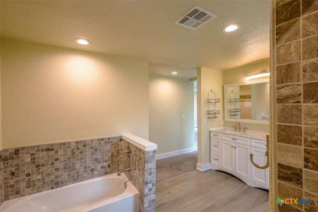 bathroom with recessed lighting, wood finished floors, vanity, visible vents, and a garden tub