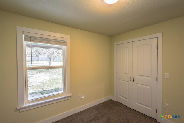 unfurnished bedroom featuring a closet, dark colored carpet, and baseboards