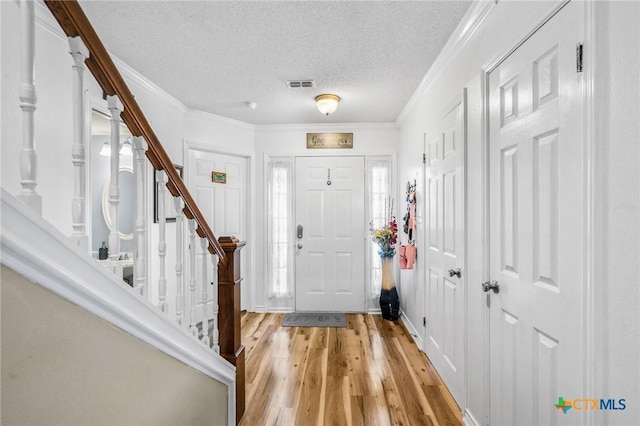 foyer featuring crown molding, light wood-style flooring, a textured ceiling, visible vents, and stairway