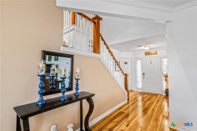 foyer featuring stairway, baseboards, crown molding, and wood finished floors