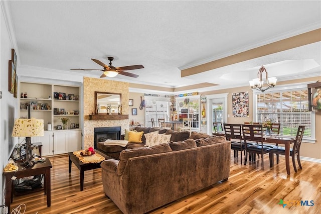 living area featuring crown molding, ceiling fan with notable chandelier, light wood finished floors, and a fireplace