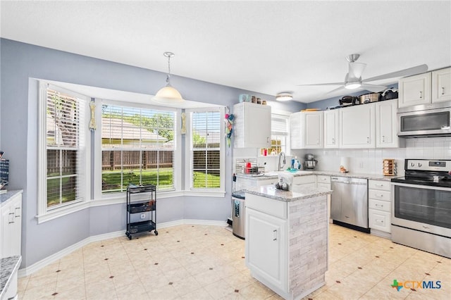kitchen featuring a wealth of natural light, white cabinets, baseboards, and appliances with stainless steel finishes