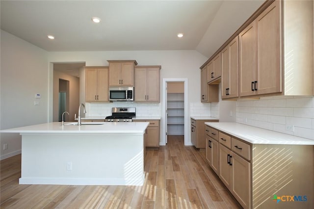 kitchen with a sink, a center island with sink, light wood-type flooring, tasteful backsplash, and appliances with stainless steel finishes