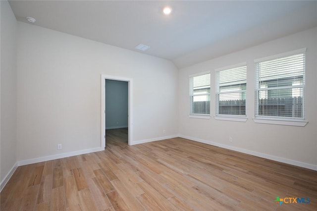 spare room featuring baseboards, lofted ceiling, and light wood-style flooring