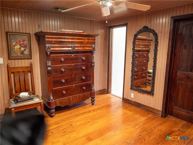 bedroom with visible vents, baseboards, a ceiling fan, wooden walls, and light wood finished floors