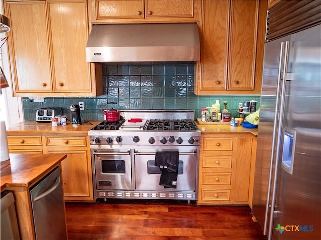 kitchen with tasteful backsplash, dark wood-style flooring, high quality appliances, wooden counters, and wall chimney exhaust hood