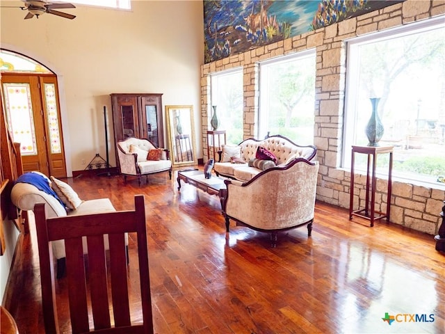 living area with wood-type flooring, a towering ceiling, and a ceiling fan