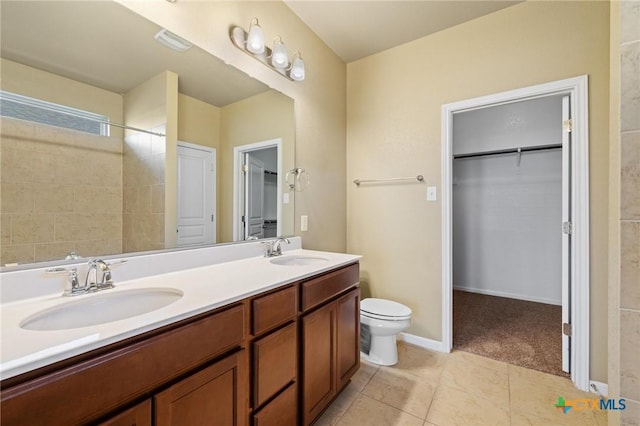 bathroom featuring a walk in closet, double vanity, toilet, and a sink