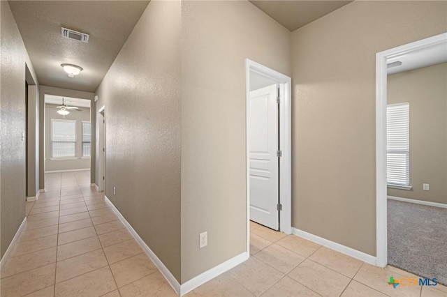 hallway featuring light tile patterned flooring, visible vents, a textured ceiling, and baseboards