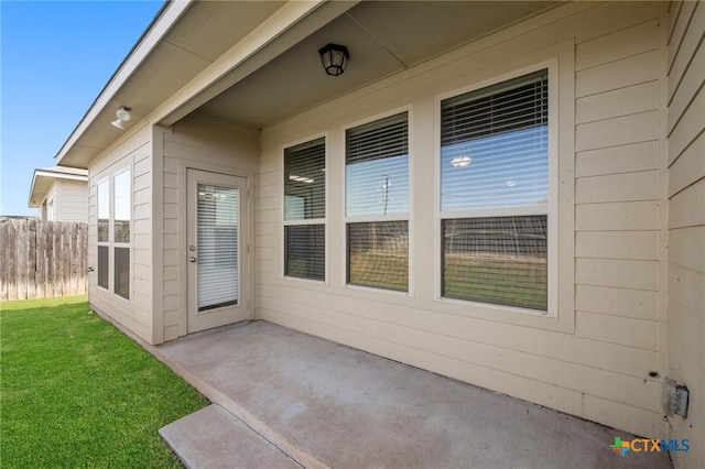 doorway to property featuring a patio area, a lawn, and fence