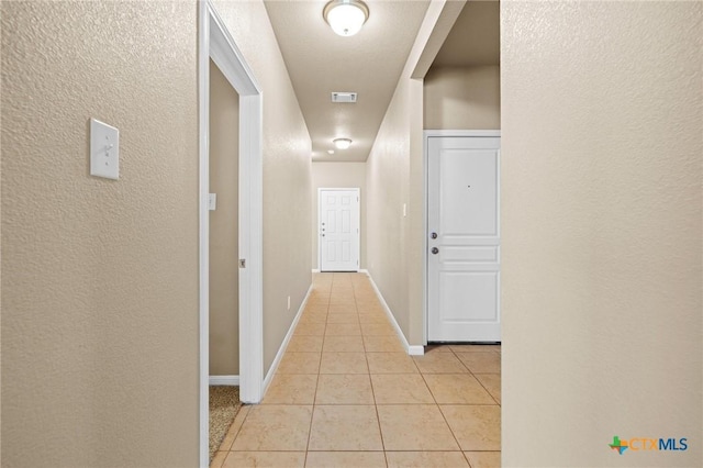 hallway with light tile patterned floors, visible vents, baseboards, and a textured wall