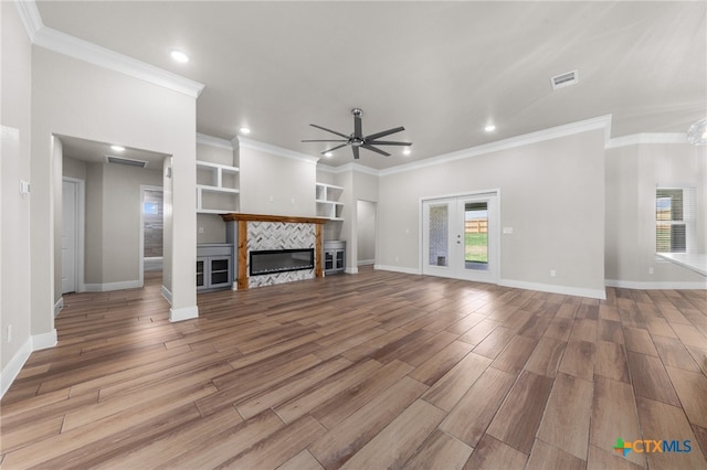 unfurnished living room featuring ceiling fan, a tiled fireplace, ornamental molding, and light hardwood / wood-style flooring