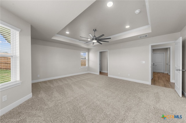 unfurnished bedroom featuring a tray ceiling, crown molding, ceiling fan, and light colored carpet