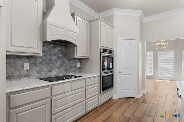 kitchen with black electric stovetop, custom range hood, stainless steel double oven, white cabinets, and light hardwood / wood-style floors