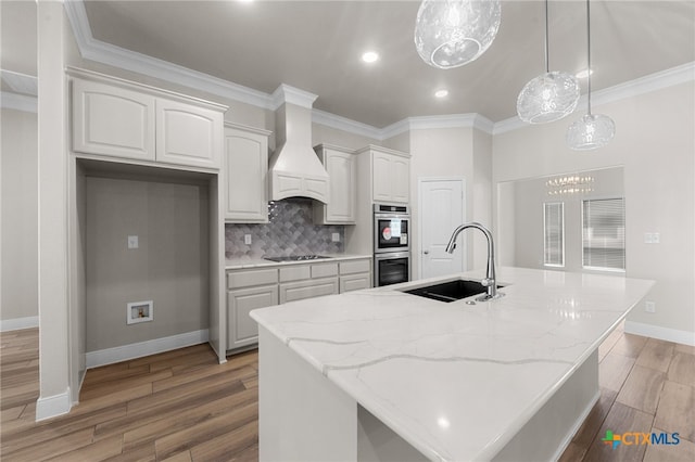 kitchen featuring light stone countertops, custom range hood, sink, light hardwood / wood-style floors, and an island with sink