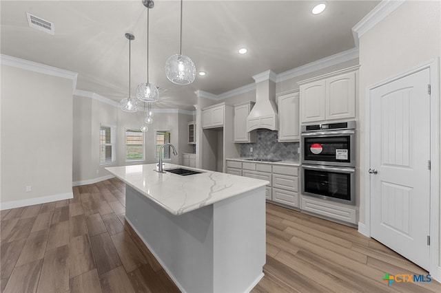 kitchen with sink, light stone counters, premium range hood, double oven, and white cabinets