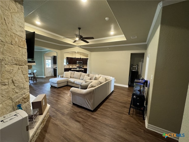 living room with a raised ceiling, dark wood-type flooring, ceiling fan, and crown molding