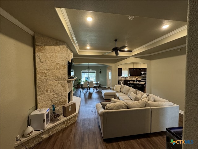 living room with crown molding, a textured ceiling, dark wood-type flooring, a tray ceiling, and ceiling fan