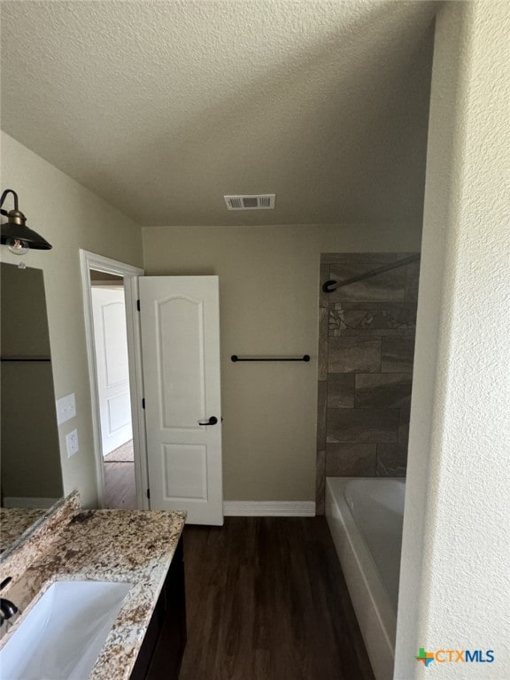 bathroom with tiled shower / bath combo, vanity, hardwood / wood-style floors, and a textured ceiling