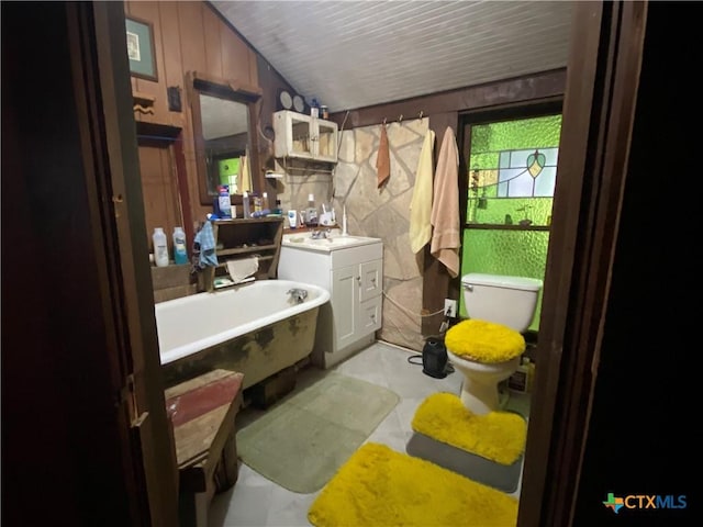 bathroom with vanity, a bathtub, wooden walls, and toilet