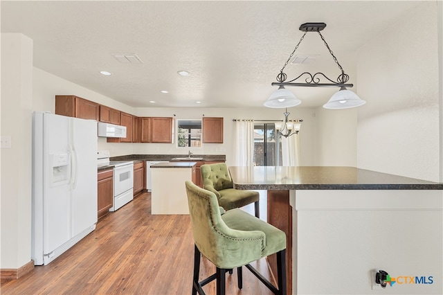 kitchen with dark hardwood / wood-style flooring, a textured ceiling, a breakfast bar area, white appliances, and decorative light fixtures