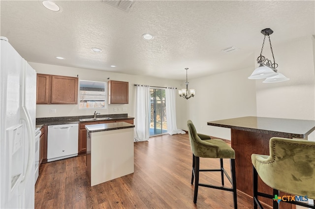 kitchen featuring dark countertops, white appliances, a kitchen island, and dark wood-style flooring