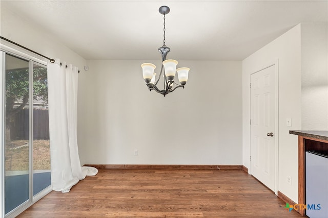 unfurnished dining area featuring a chandelier, baseboards, and wood finished floors