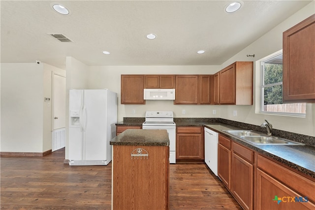 kitchen with white appliances, visible vents, dark wood finished floors, a center island, and a sink