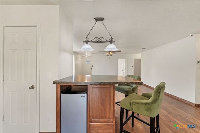 kitchen with baseboards, brown cabinetry, dark countertops, wood finished floors, and fridge