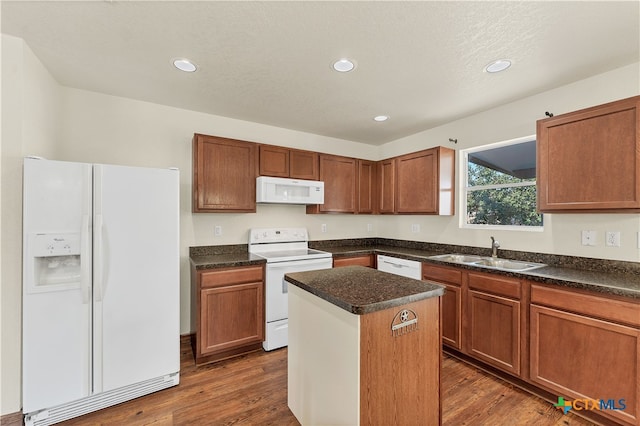 kitchen with white appliances, dark wood finished floors, dark countertops, a center island, and a sink