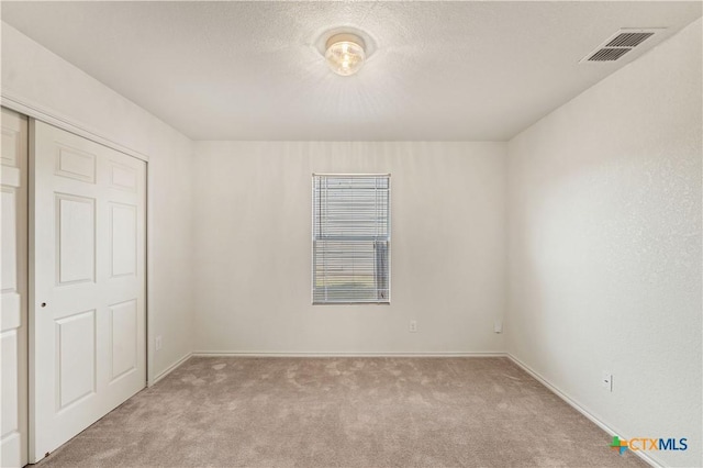 carpeted spare room featuring baseboards, visible vents, and a textured ceiling