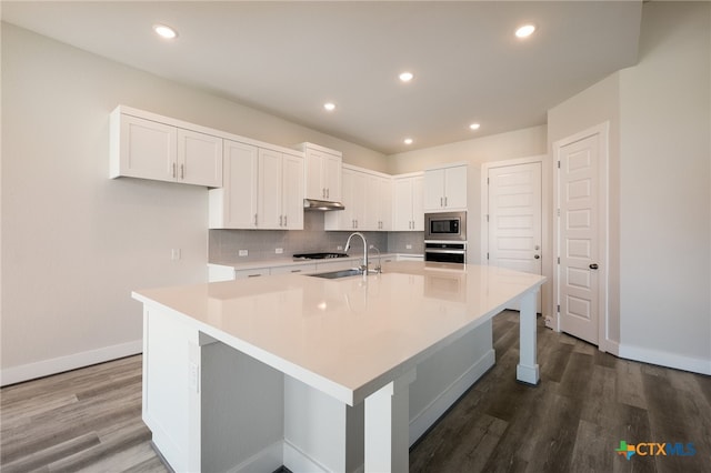 kitchen with white cabinetry, hardwood / wood-style floors, stainless steel appliances, and an island with sink