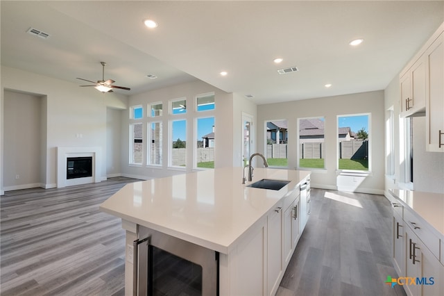 kitchen with a kitchen island with sink, wine cooler, white cabinetry, sink, and light hardwood / wood-style flooring