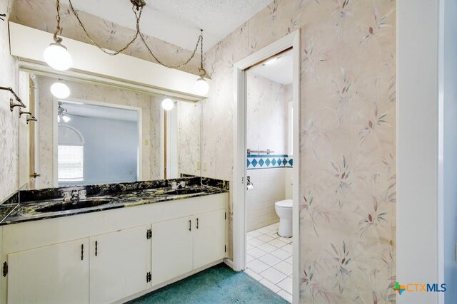 bathroom featuring tile patterned flooring, ceiling fan, a textured ceiling, vanity, and toilet