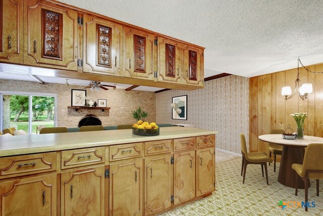 kitchen featuring a fireplace, a textured ceiling, decorative light fixtures, kitchen peninsula, and ceiling fan with notable chandelier