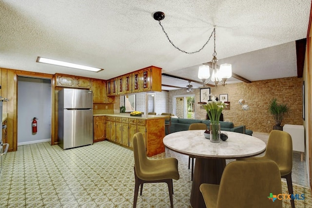 kitchen featuring ceiling fan with notable chandelier, kitchen peninsula, hanging light fixtures, a textured ceiling, and stainless steel fridge