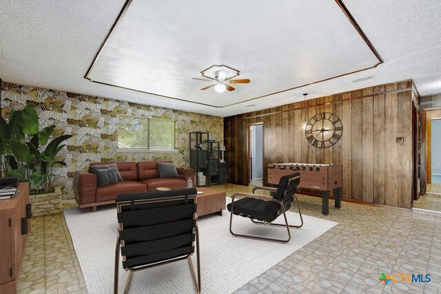 living room featuring ceiling fan, wooden walls, and a textured ceiling