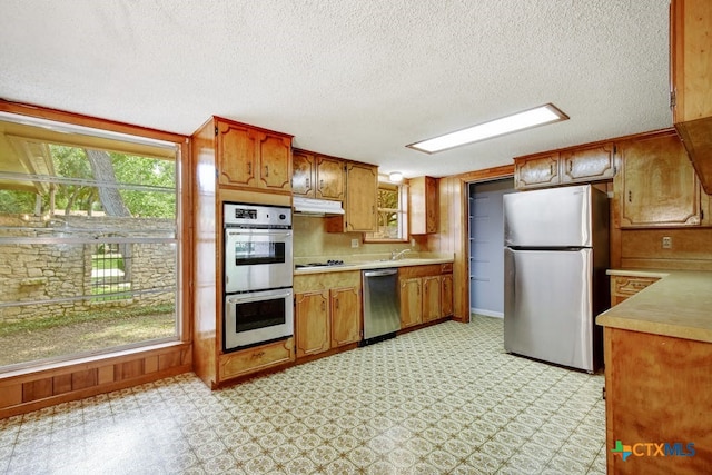 kitchen featuring stainless steel appliances, wood walls, a textured ceiling, and sink