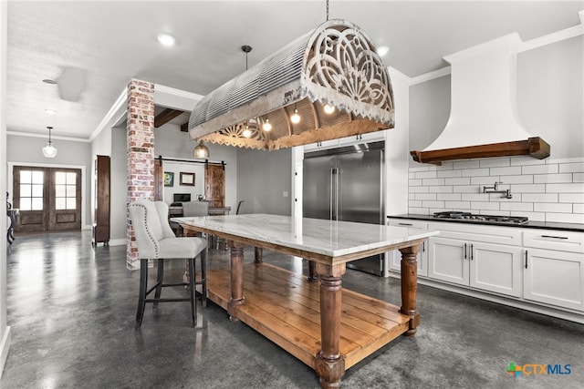 kitchen featuring appliances with stainless steel finishes, hanging light fixtures, backsplash, white cabinets, and a barn door