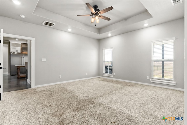 carpeted spare room featuring a raised ceiling and ceiling fan