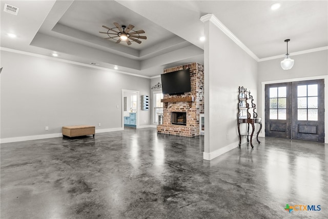 foyer entrance with concrete flooring, ceiling fan, a raised ceiling, a brick fireplace, and french doors