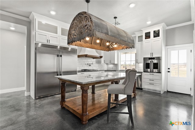 kitchen with appliances with stainless steel finishes, white cabinetry, backsplash, custom range hood, and decorative light fixtures