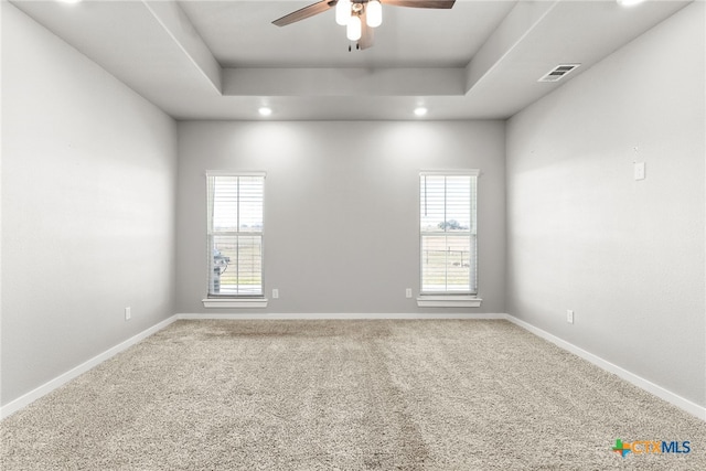 carpeted empty room with a raised ceiling, a healthy amount of sunlight, and ceiling fan