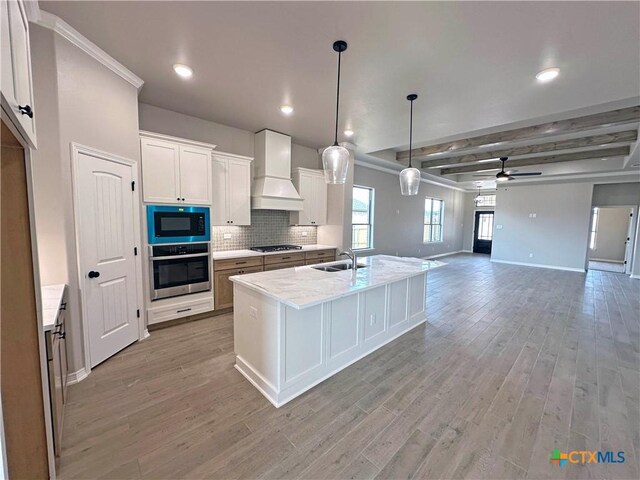 kitchen with light wood-style flooring, a sink, appliances with stainless steel finishes, tasteful backsplash, and custom range hood