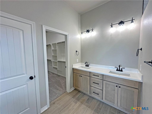 full bathroom featuring a walk in closet, double vanity, a sink, and wood finished floors